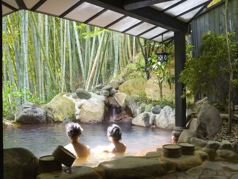 Women bathing in an outdoor pool in Japan, with bamboo in the background. 