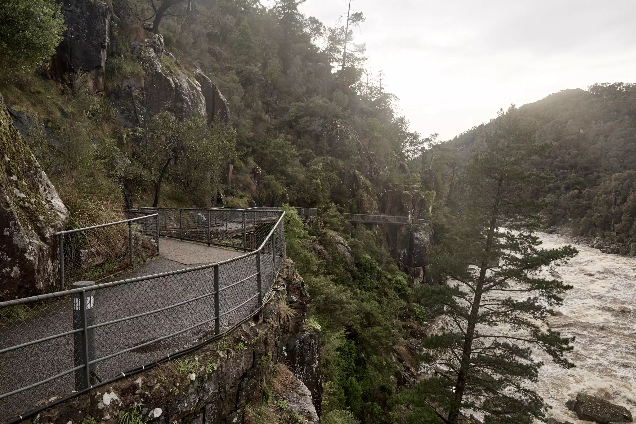 A black path next to a river and green hills