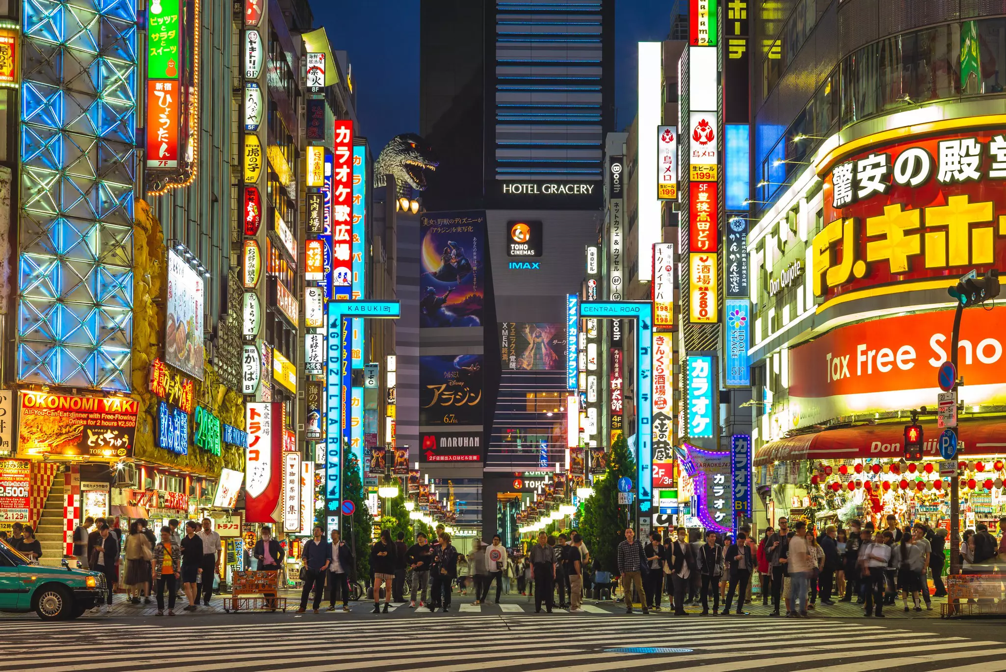 Godzilla head above illuminated signs on a busy Shinjuku street at night