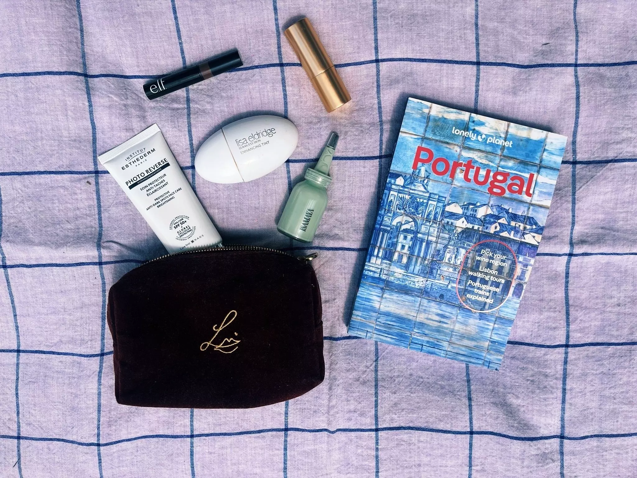 A travel guidebook and beauty products are laid out on a blue check cloth