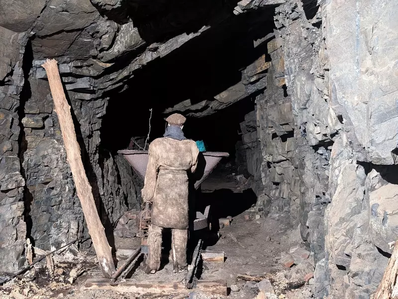 Recreation of worker in overcoat and hat, holding a lantern near unfinished stone tunnel.