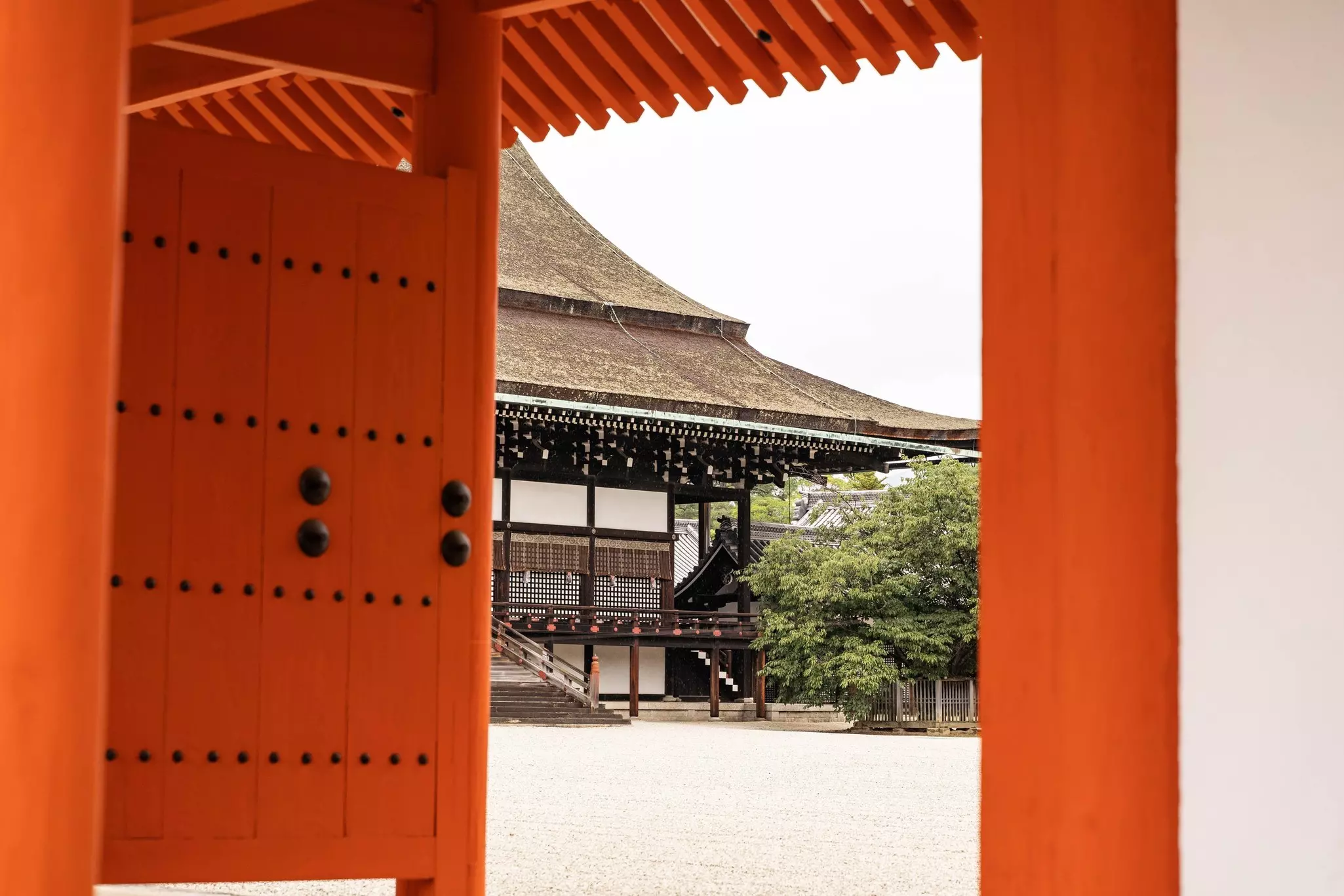 A red gate frames the view of a traditional structure in Japan.