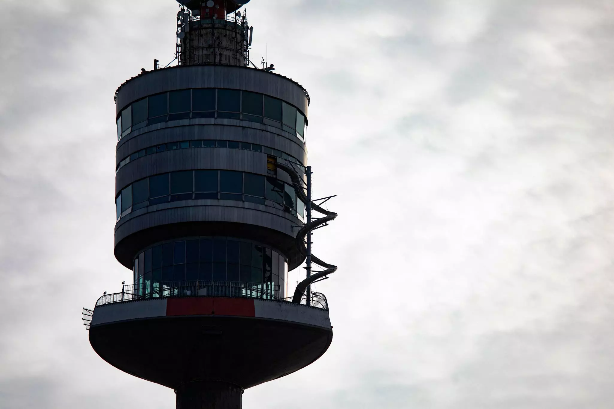 Enclosed pavilions at the top of a narrow tower are seen silhouetted against a gray sky. A curling slide is attached to the tower.