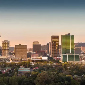 City skyline of office towers, including a green glass tower, above dense trees in morning light, Pretoria, South Africa
