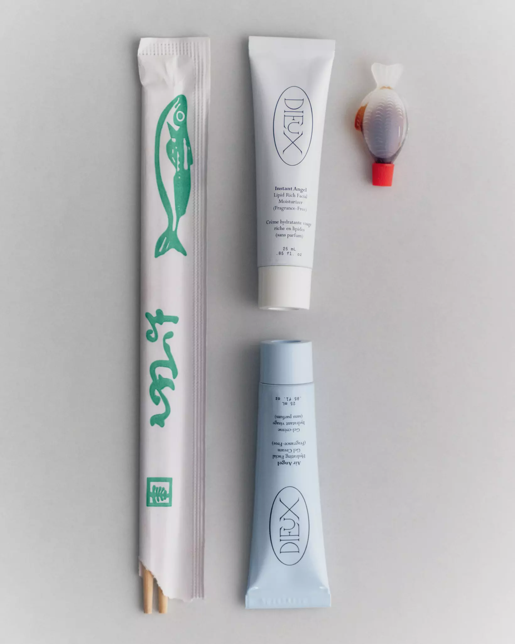 Two mini skincare products in tubes are lined up against a soy sauce in a fish bottle and chopsticks for scale