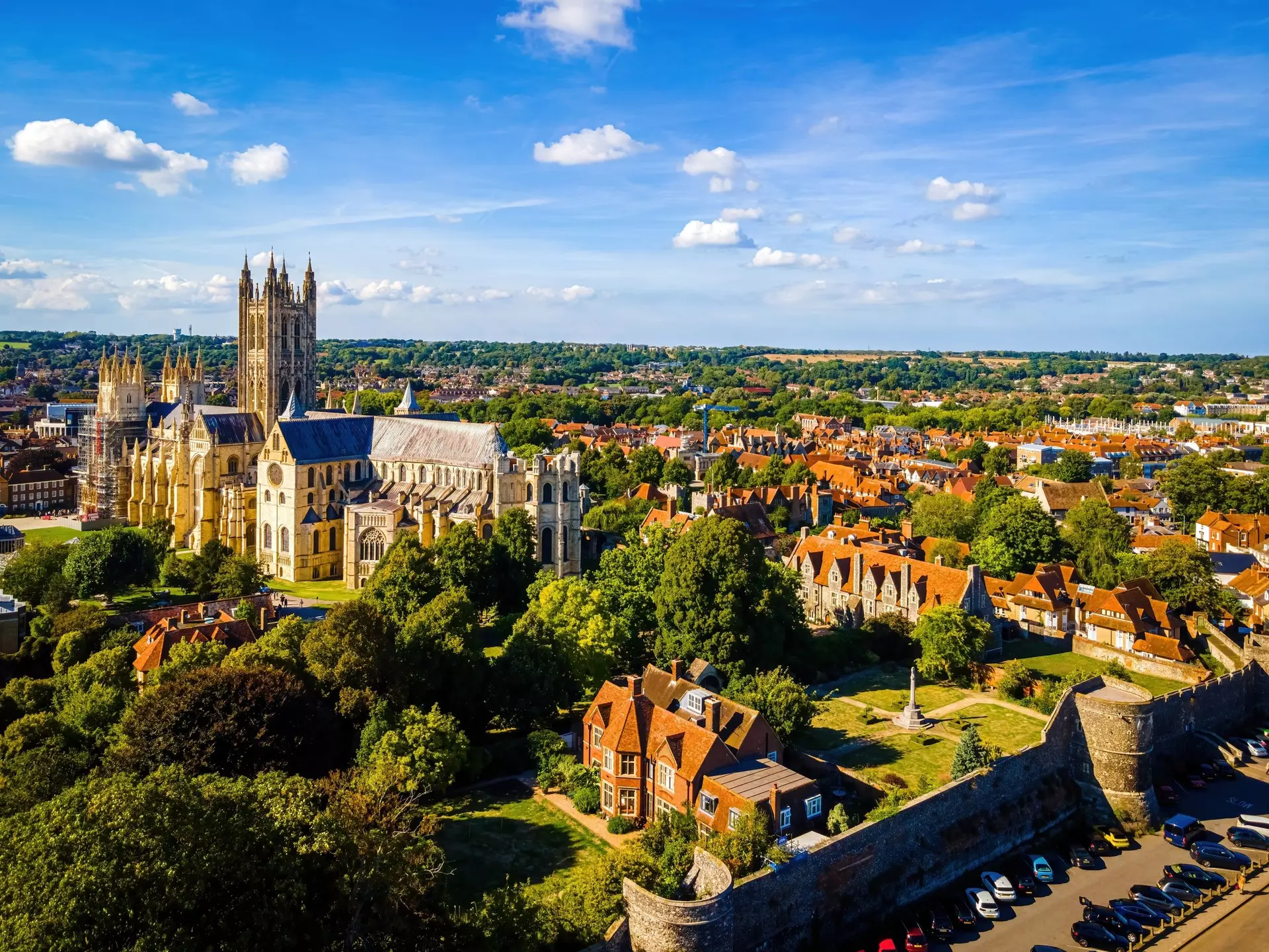 Aerial view of a tree-filled historic town with stone cathedral to the left and red-roofed buildings in the foreground and continuing into the distance on a sunny day.