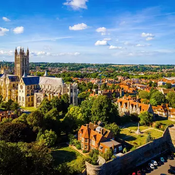 Aerial view of a tree-filled historic town with stone cathedral to the left and red-roofed buildings in the foreground and continuing into the distance on a sunny day.