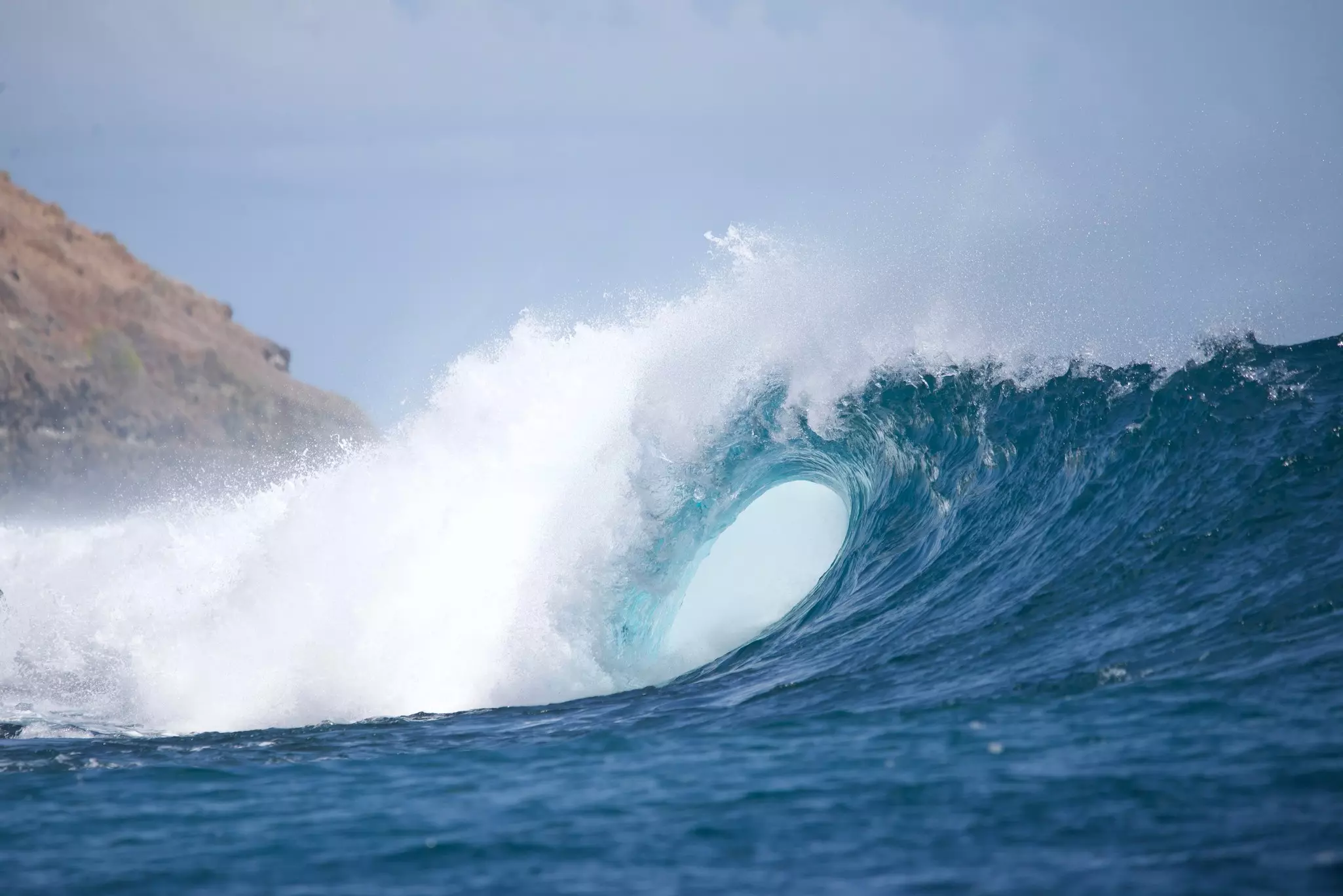 A perfectly formed barrel wave throws off white surf.