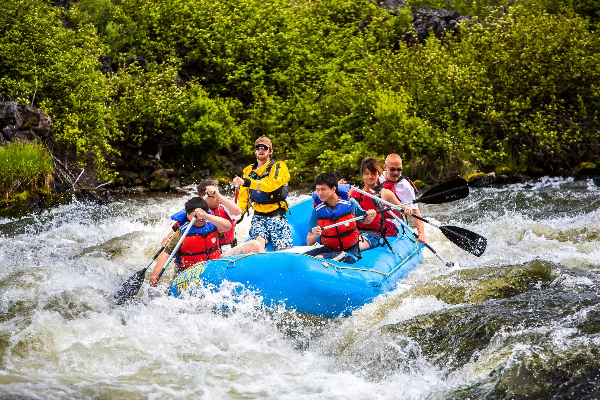 A group of people white water rafting in a rubber raft on the Deschutes River at  Big Eddy rapid - a class 4 rapid - near Bend.