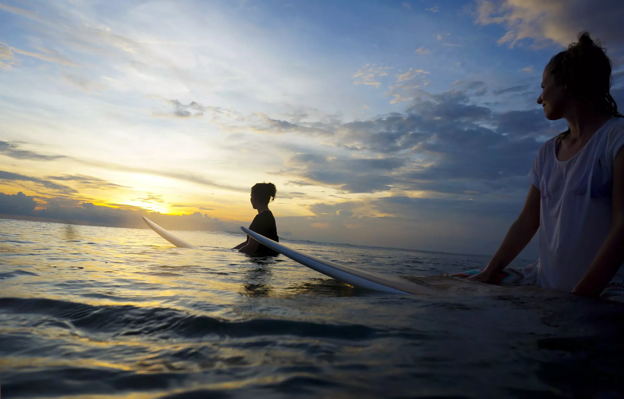 Two female surfers in the water watching the sun at Canggu