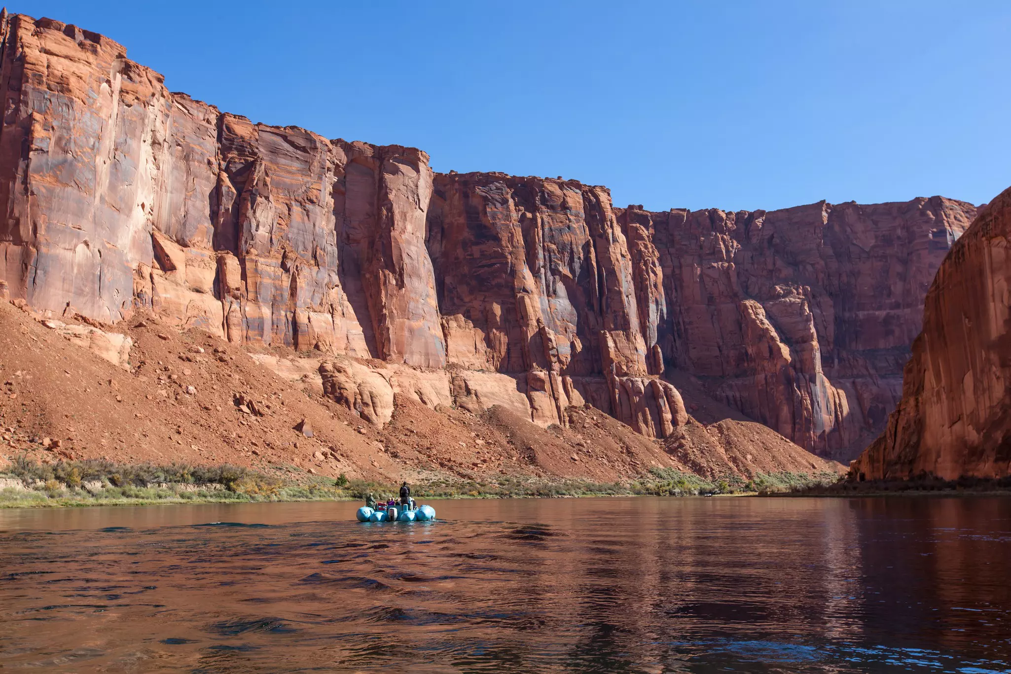 Rafting on a calm area of the Colorado River through Horseshoe Bend past massive cliffs of the gorge on a clear sunny day, Arizona