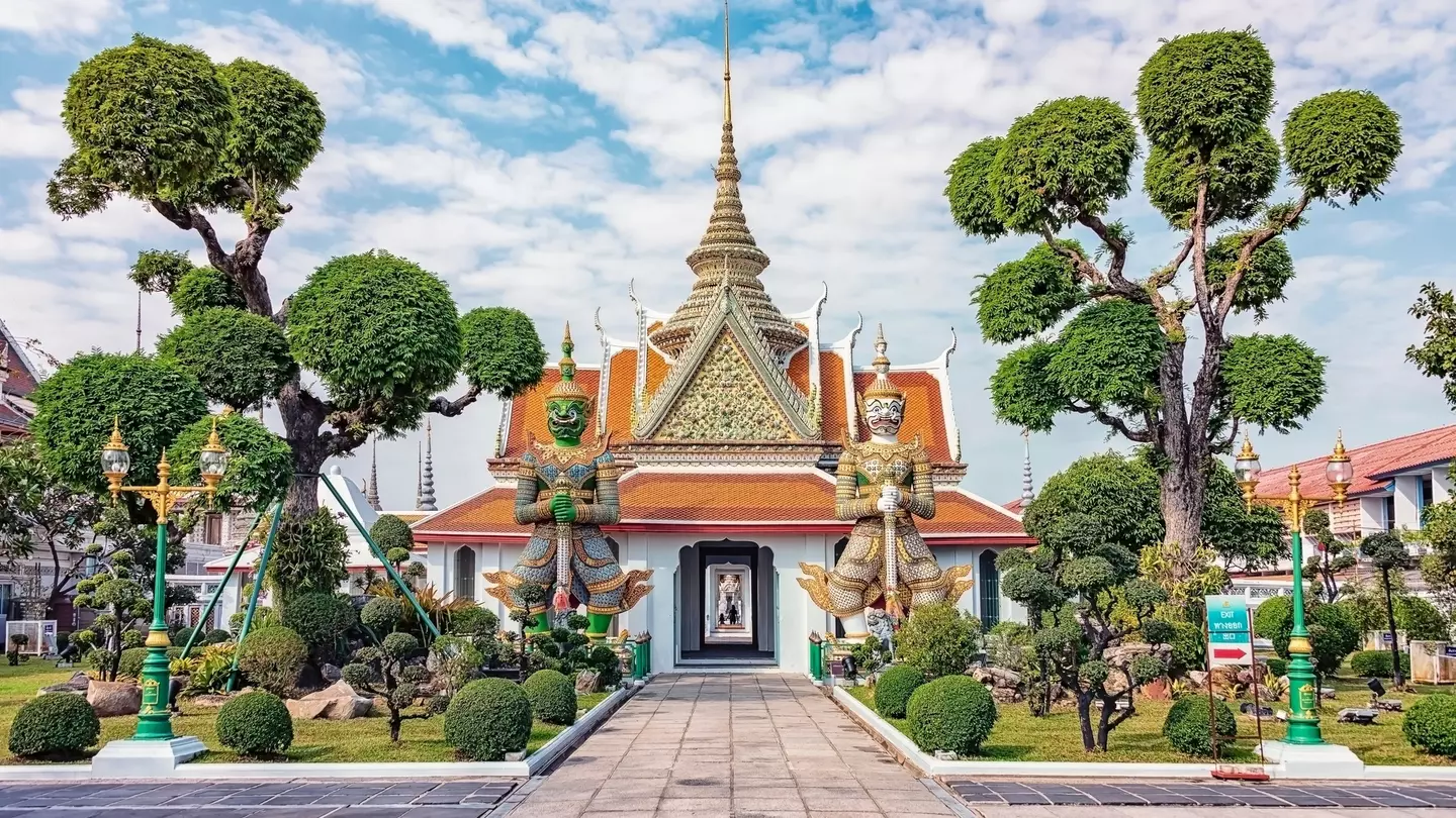 Guardian statues at Wat Arun in Bangkok, Thailand, flanked by rounded trees.