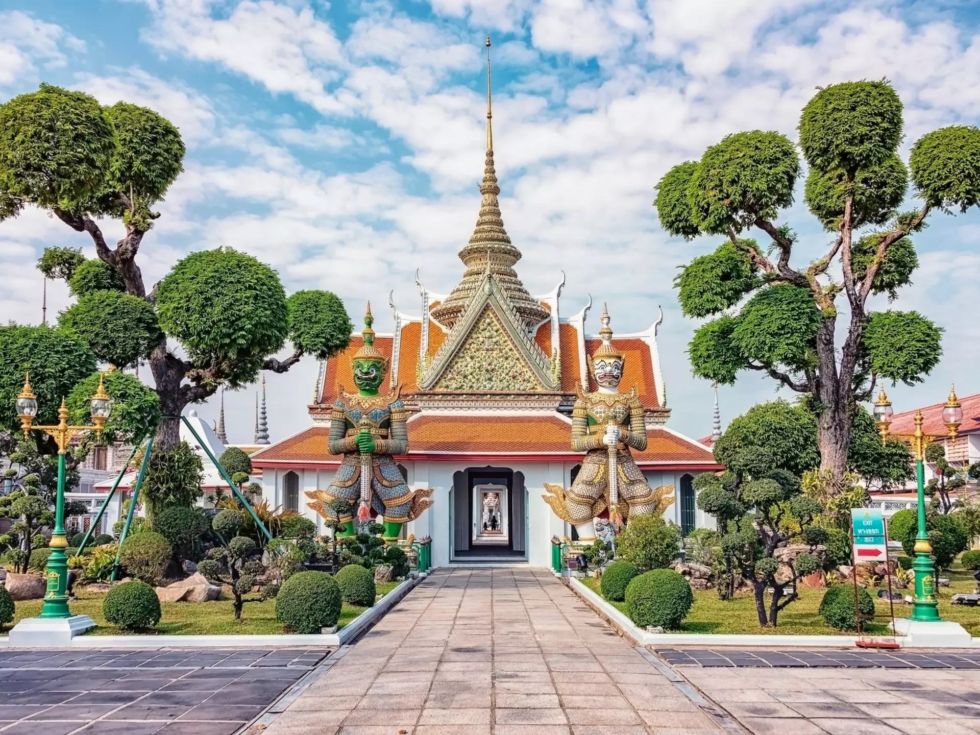 Guardian statues at Wat Arun in Bangkok, Thailand, flanked by rounded trees.