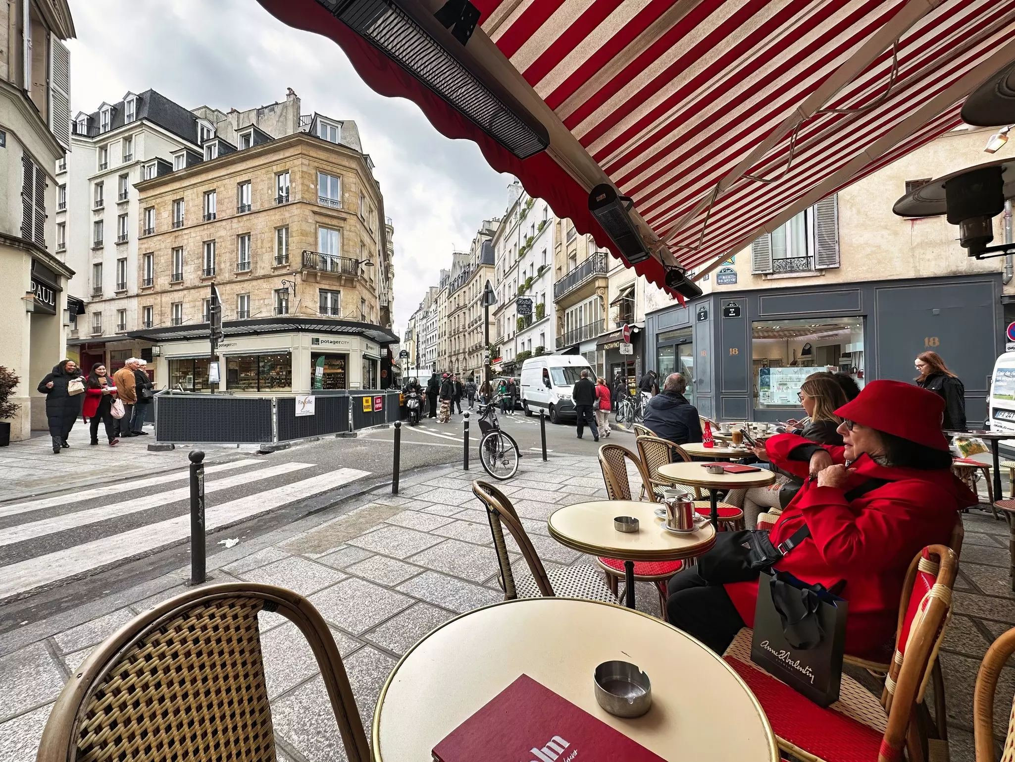 A woman in red is sitting at a table under the awning of a sidewalk cafe in Paris.