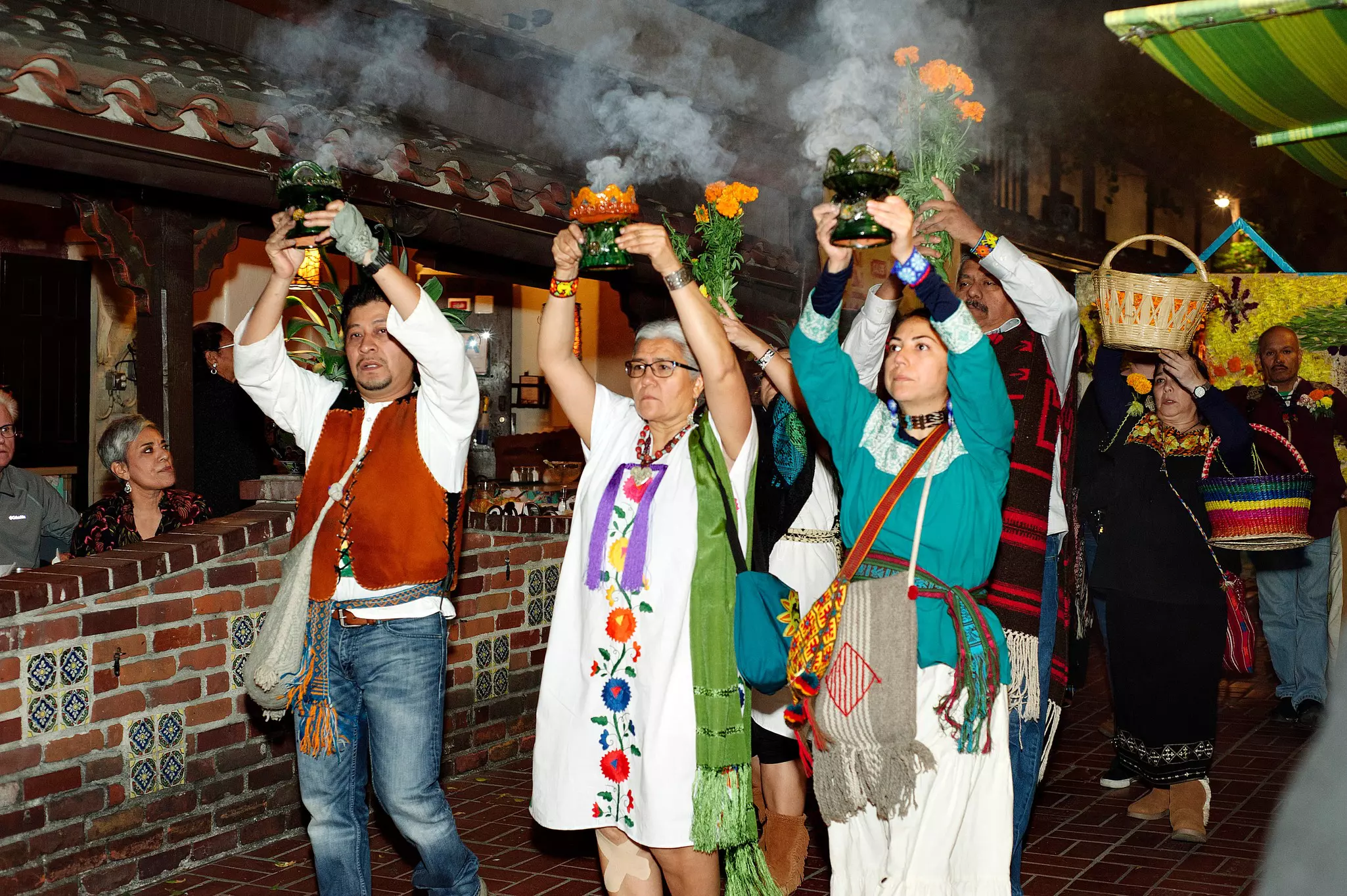 Group of people walking down the street holding marigolds and smudge sticks in the air