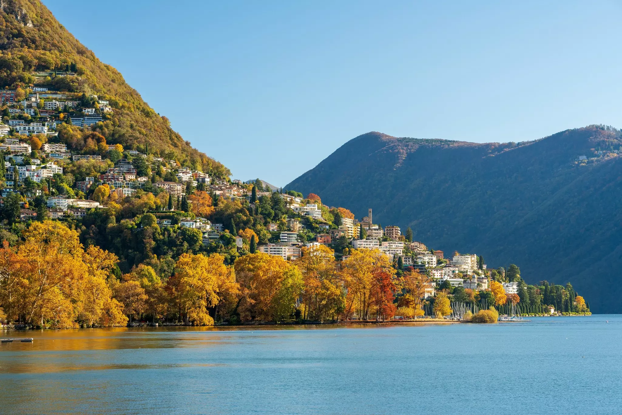 A hillside village on a lake surrounded by colorful fall foliage and mountains