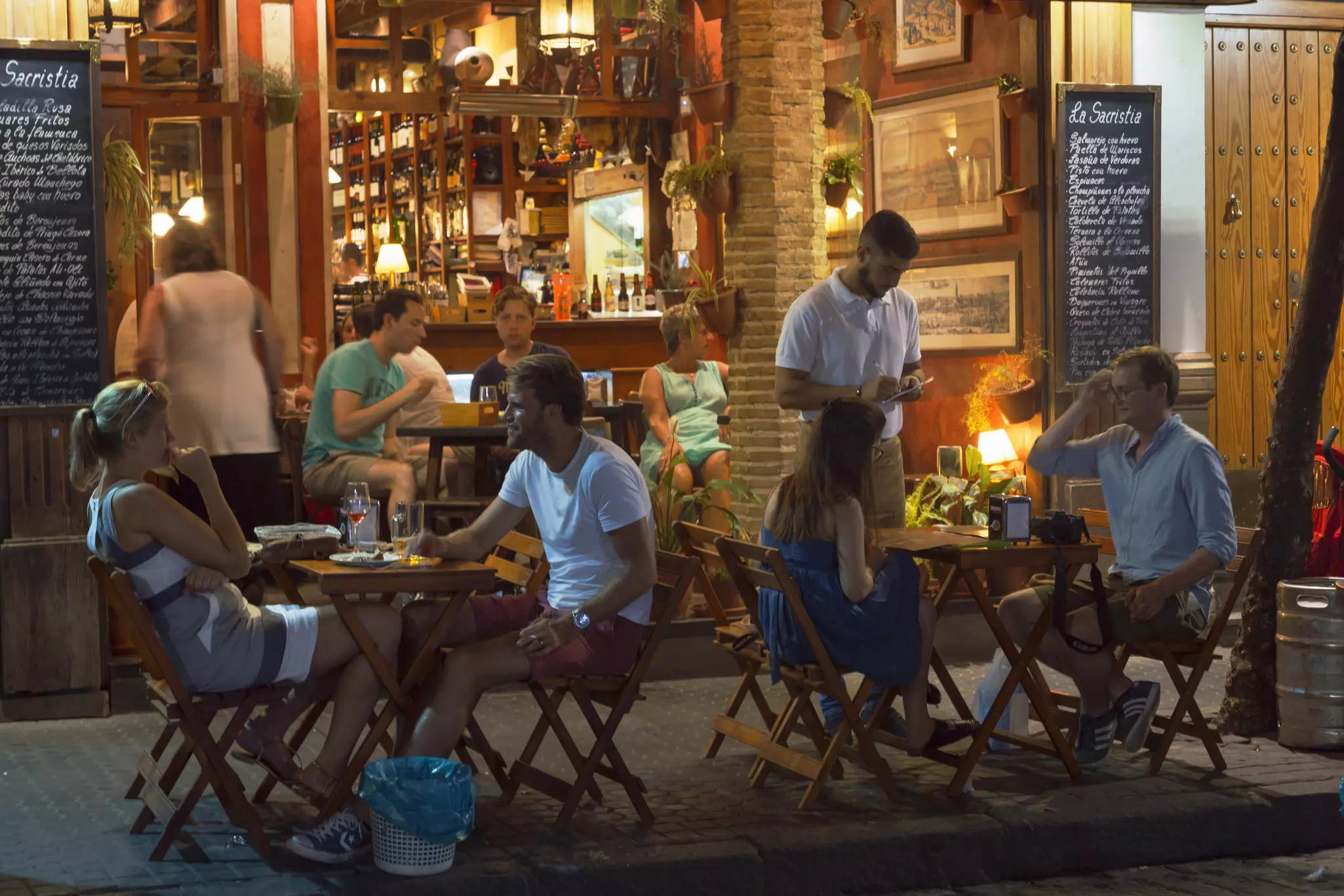 People sit at sidewalk tables in front of a cafe.