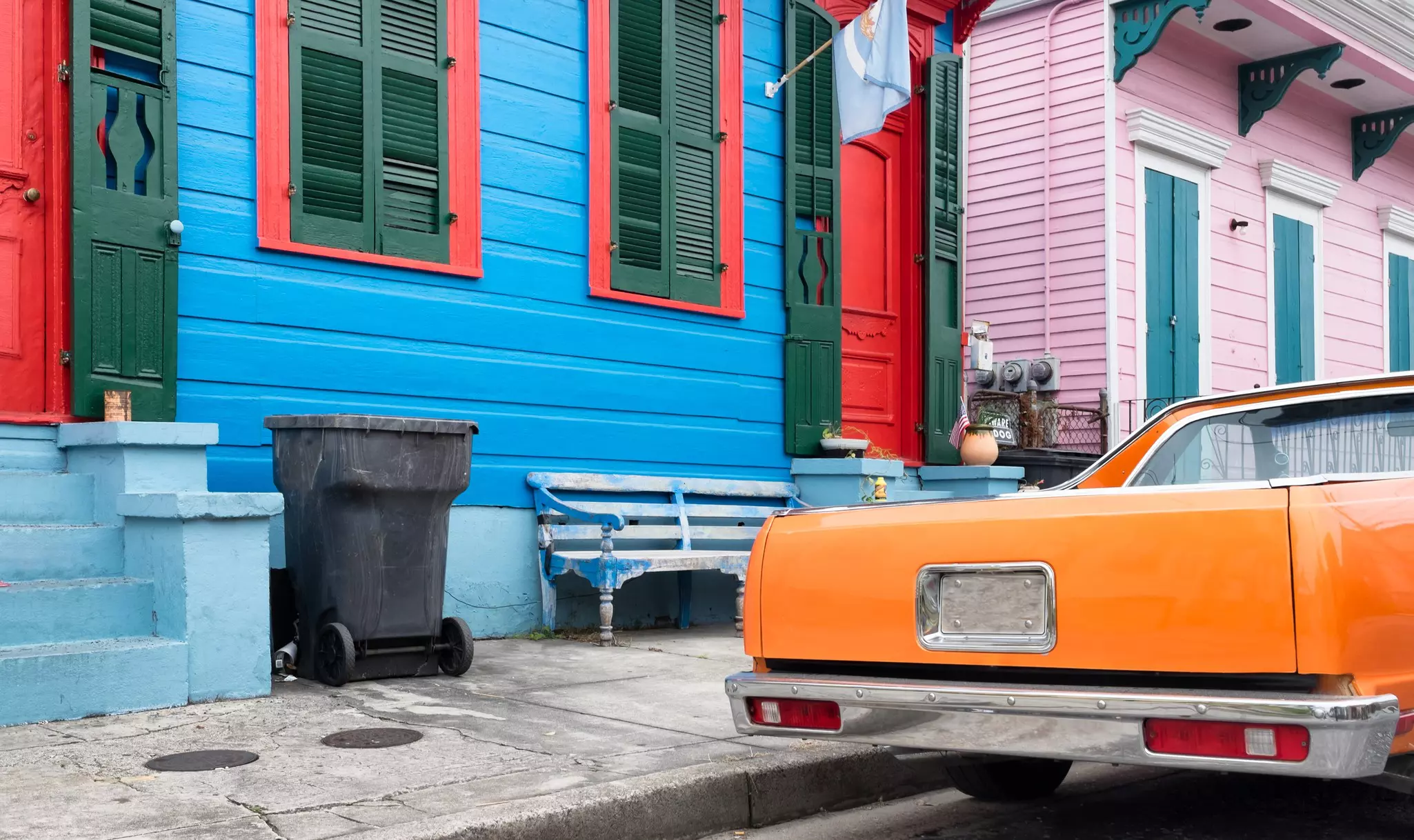 Colorful painted houses and a classic orange car parked on a Bywater block. 
