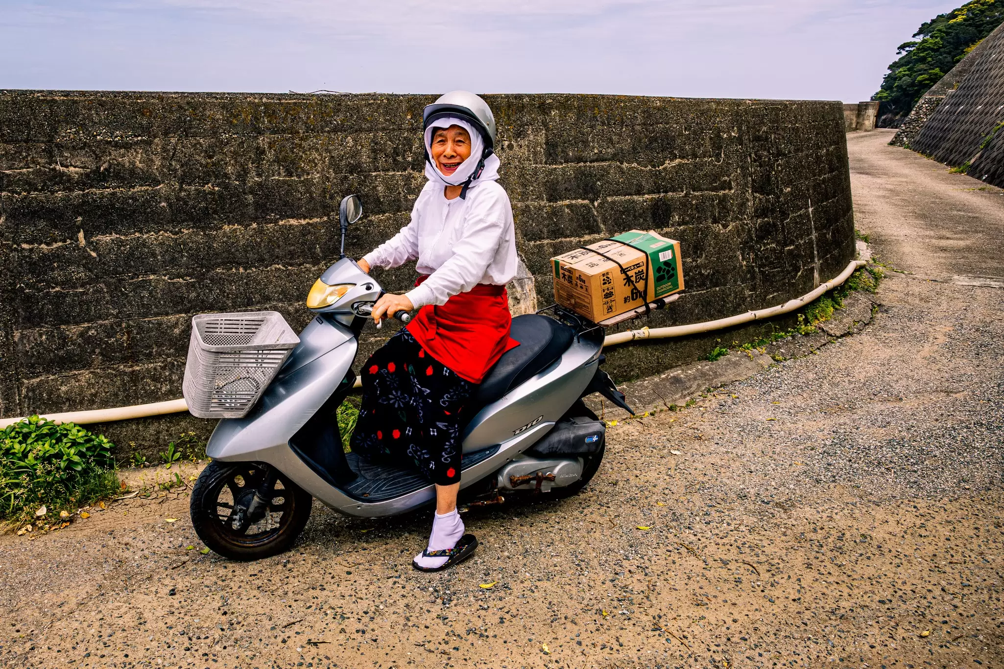 A person on a scooter smiles; a cardboard box labeled as charcoal strapped to the back.