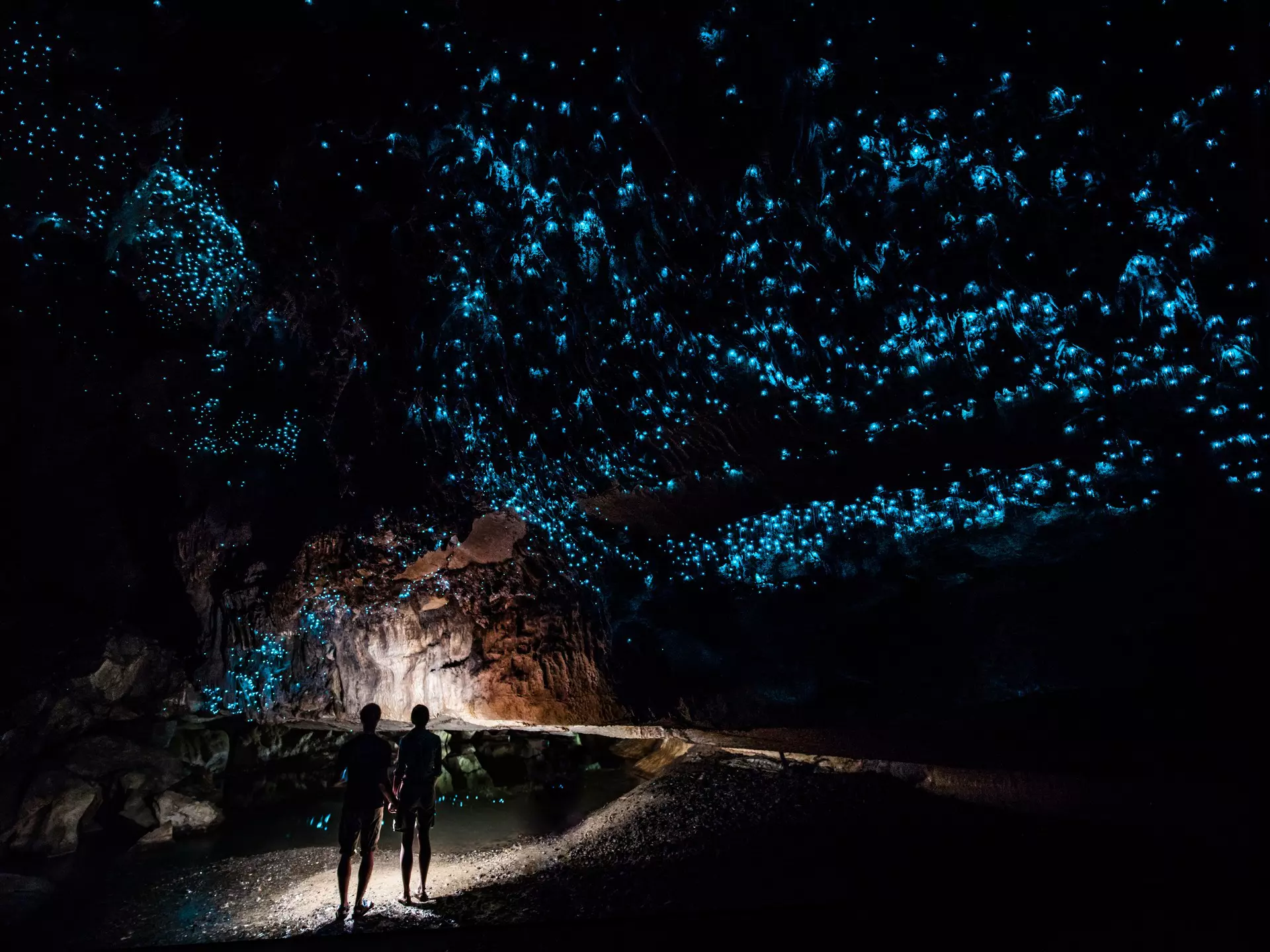 Two people in a dark cave that has blue iridescent spots on the ceiling.