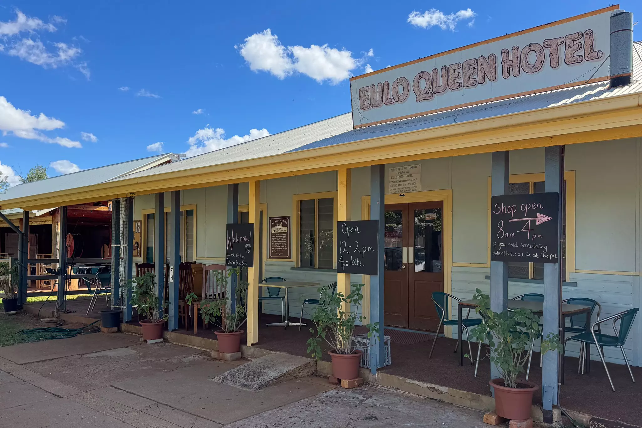 The exterior of a low-rise hotel with tables and chairs on its porch.
