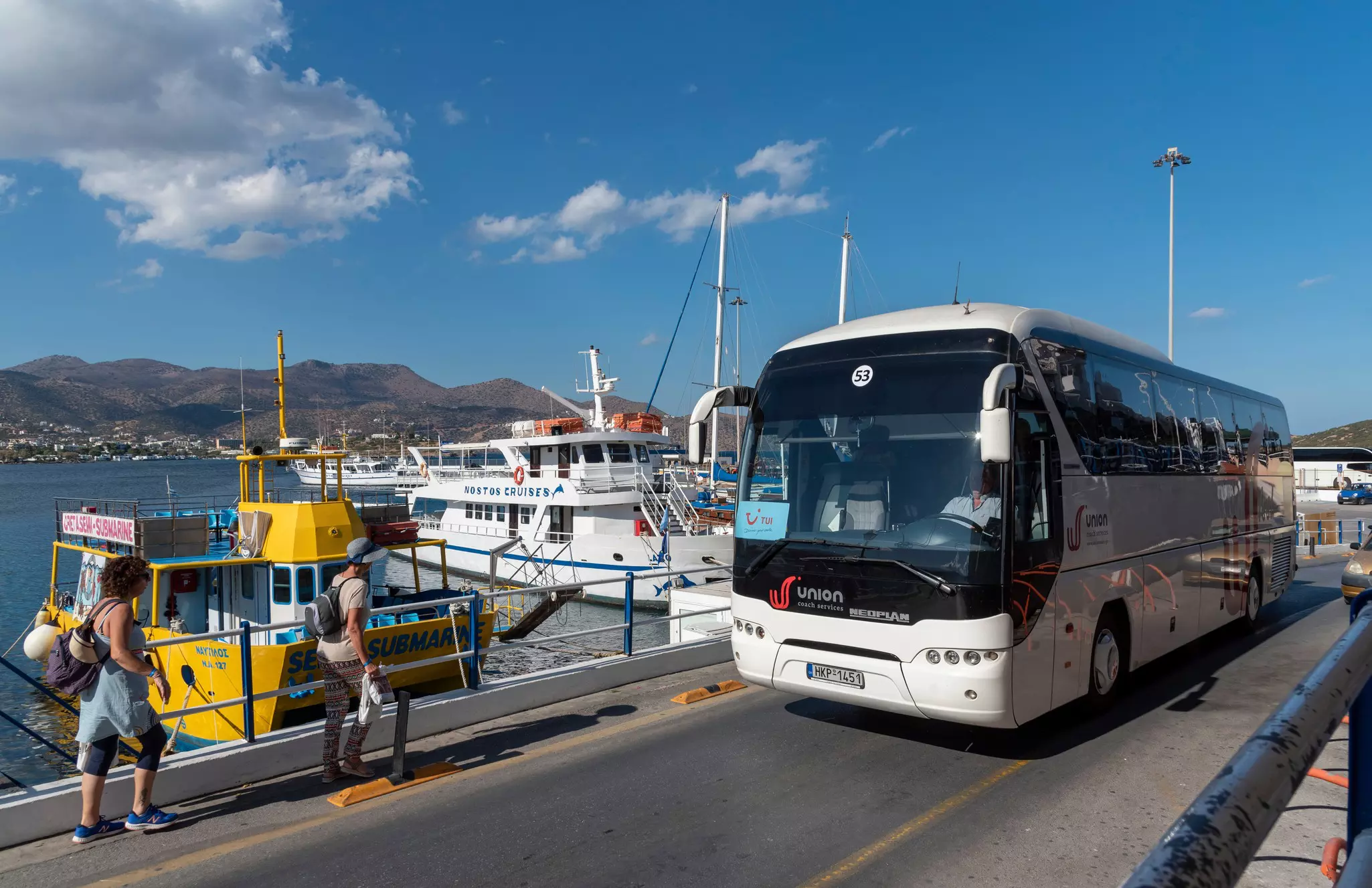 The Port  at Agios Nikolaos with boats berthed alongside the harbour and a tour bus departing the port area.