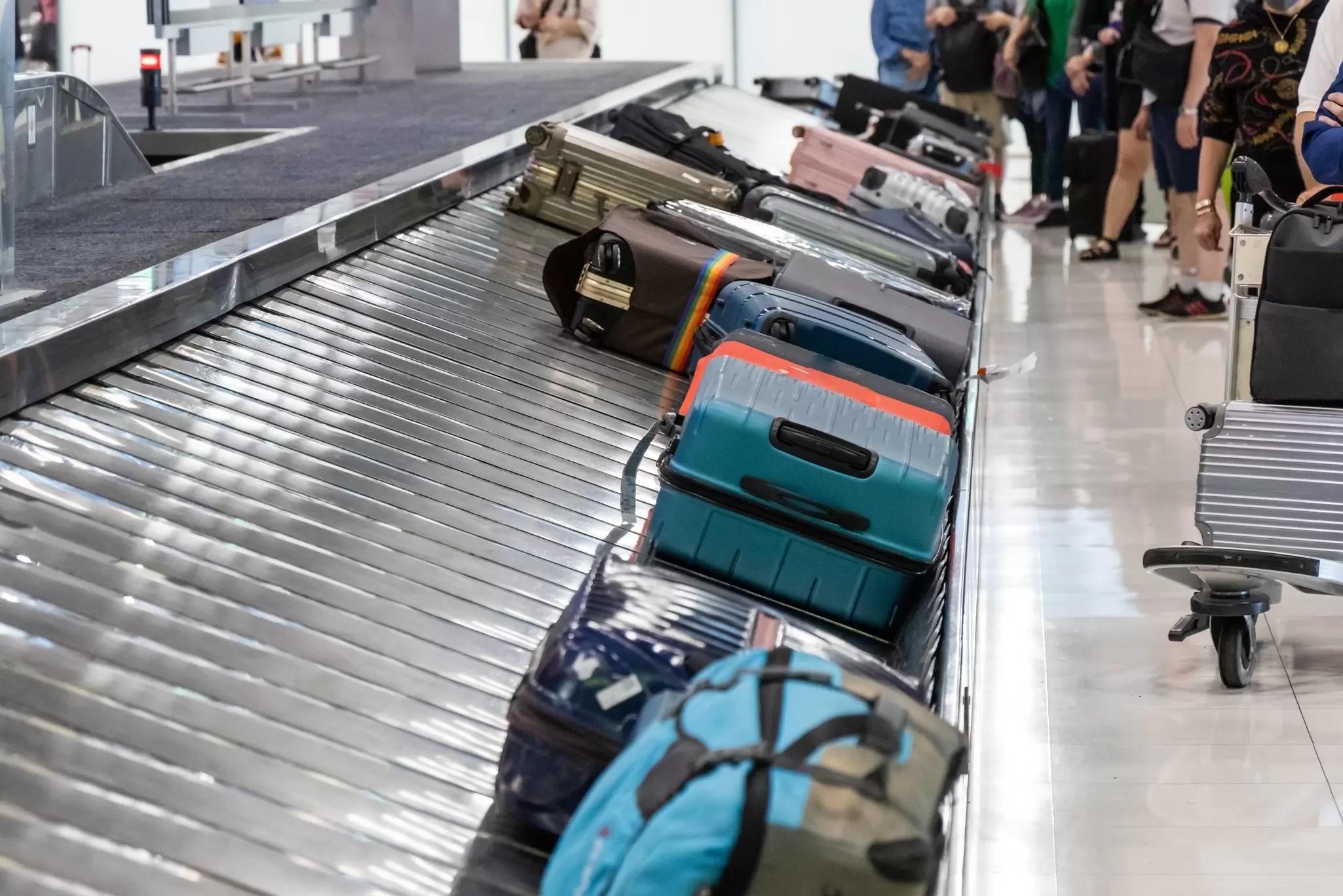 Baggage luggage at airport arrival carousel with passengers awaiting to claim their suitcases.