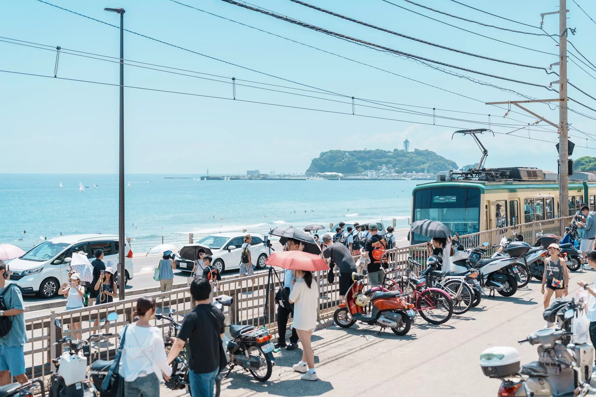 People and cars pack a busy road, railway line and promenade by the sea.