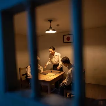 A lit diorama seen through bars shows figures around a table in a jail room.