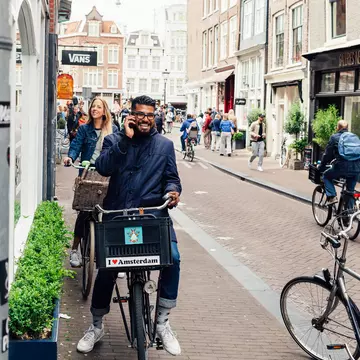 AMSTERDAM, NETHERLANDS - MAY 23, 2015: Young an happy couple on bikes on a street in Amsterdam accidentally looking into camera, happy Amsterdammers , License Type: media, Download Time: 2025-12-12T11:40:23.000Z, User: pinkjozie64, Editorial: true, purchase_order: 65020 - Marketing or Sales - this includes sponsored articles, job: Global Publishing WIP (for books) , client: Amsterdam 14, other: Jo-anne Riddell