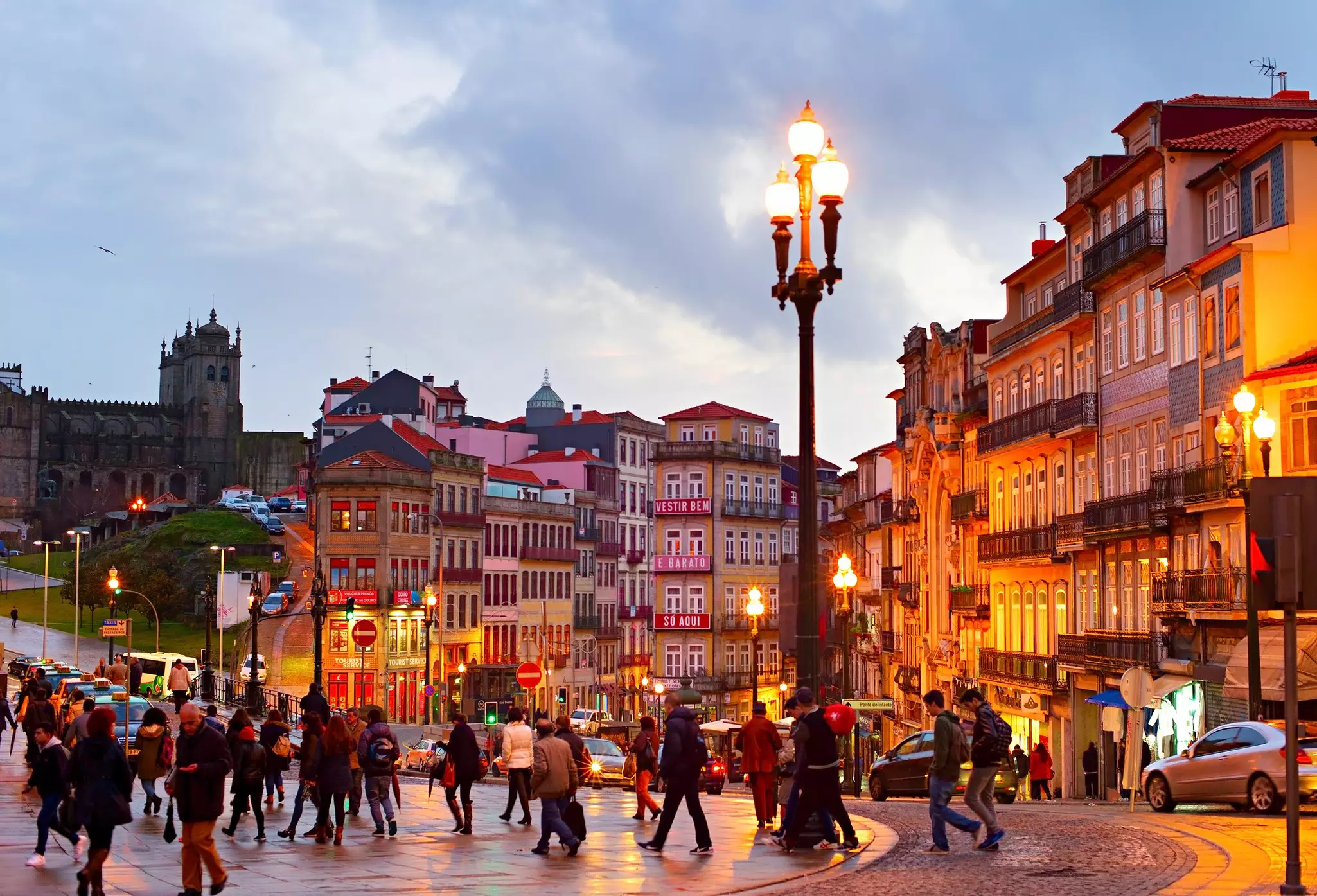 People walking through a large square after dusk with streetlights on.