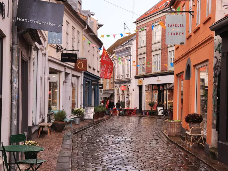 A street with cobblestones lined with two-story buildings and a sharp turn at the end.