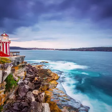 A red-and-white striped lighthouse on a sandstone headland above breaking surf under storm clouds.