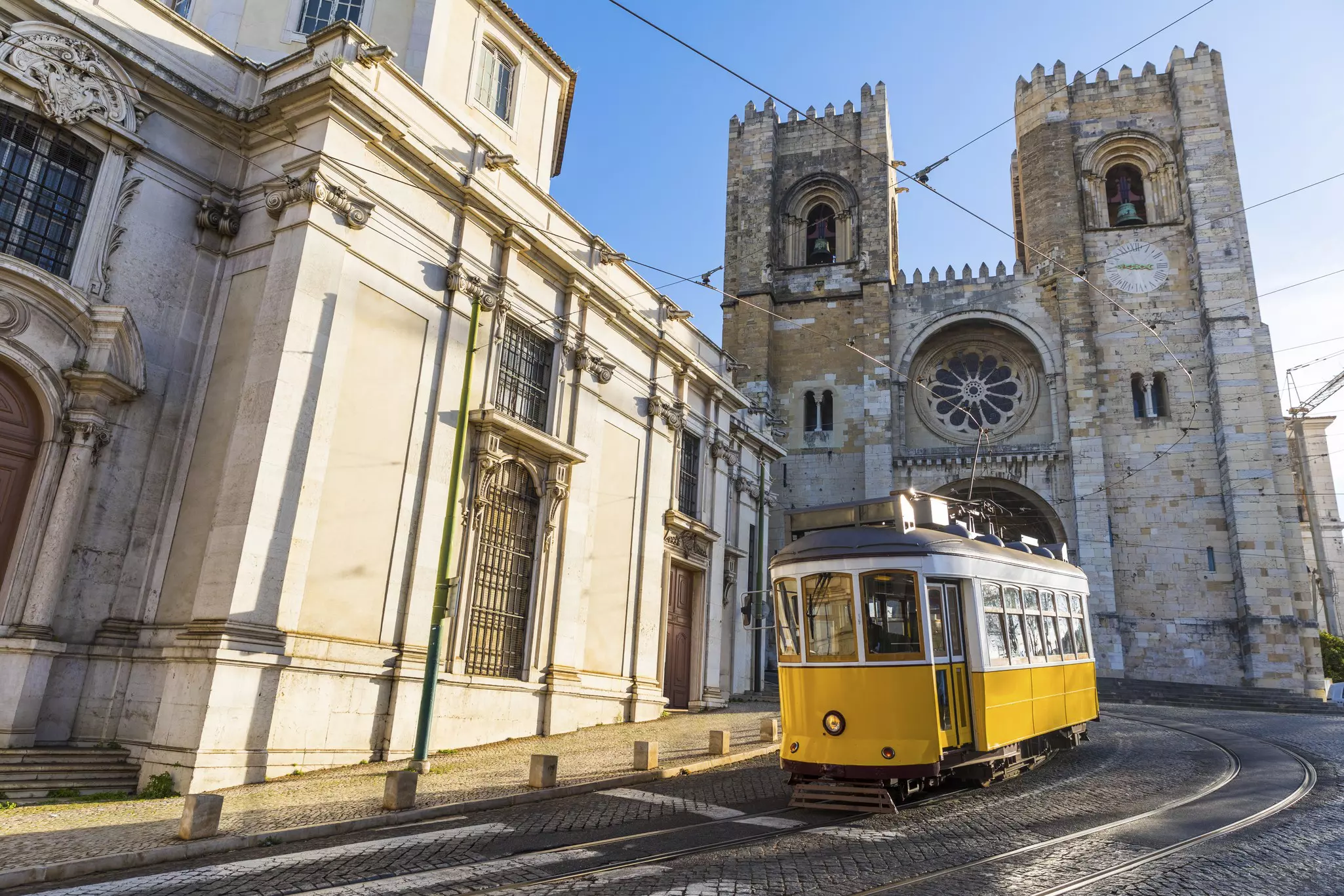 A traditional yellow tram passes in front of a large cathedral with Gothic features and a rose window.