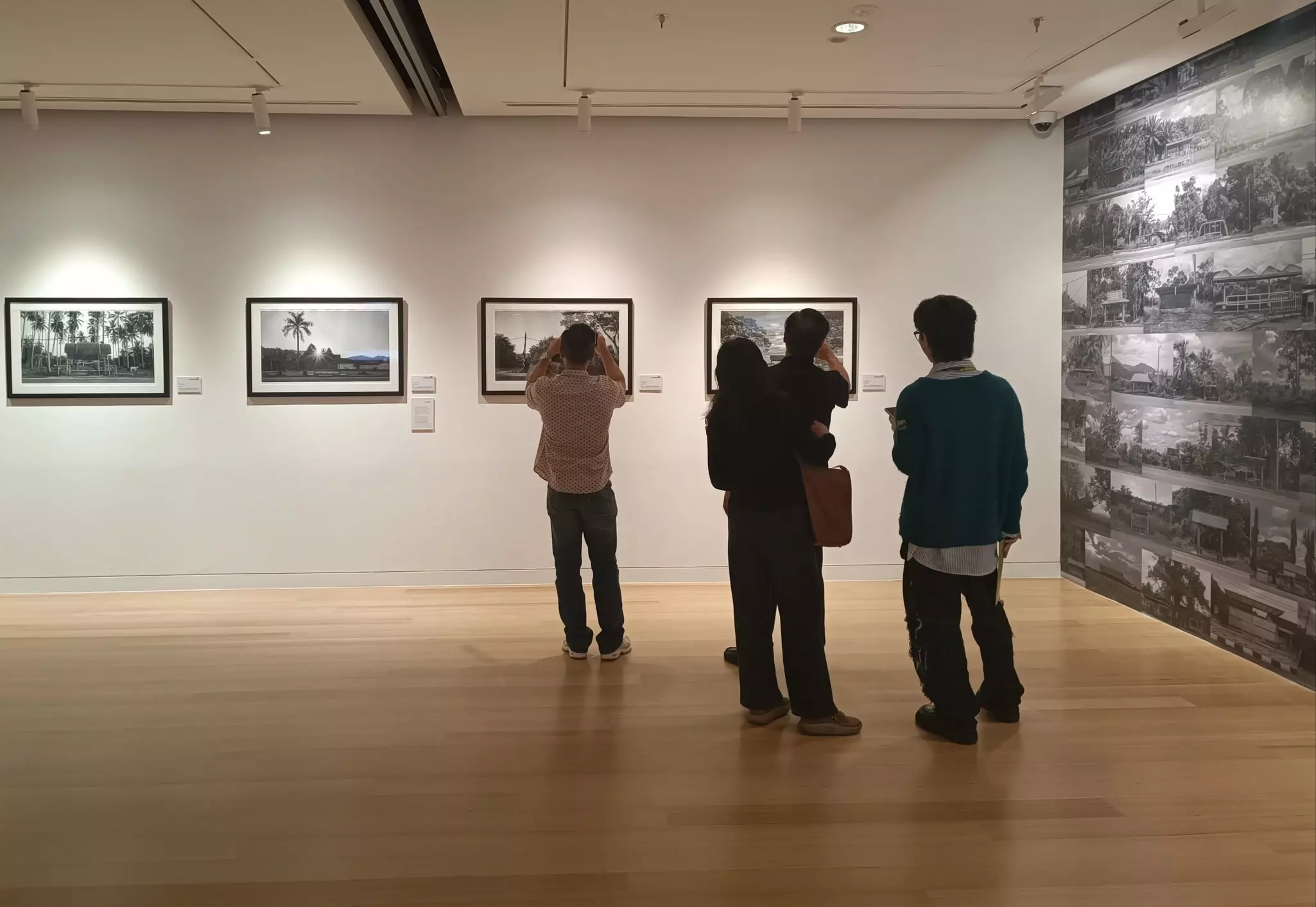 People in a gallery admire photographs mounted on a white wall.