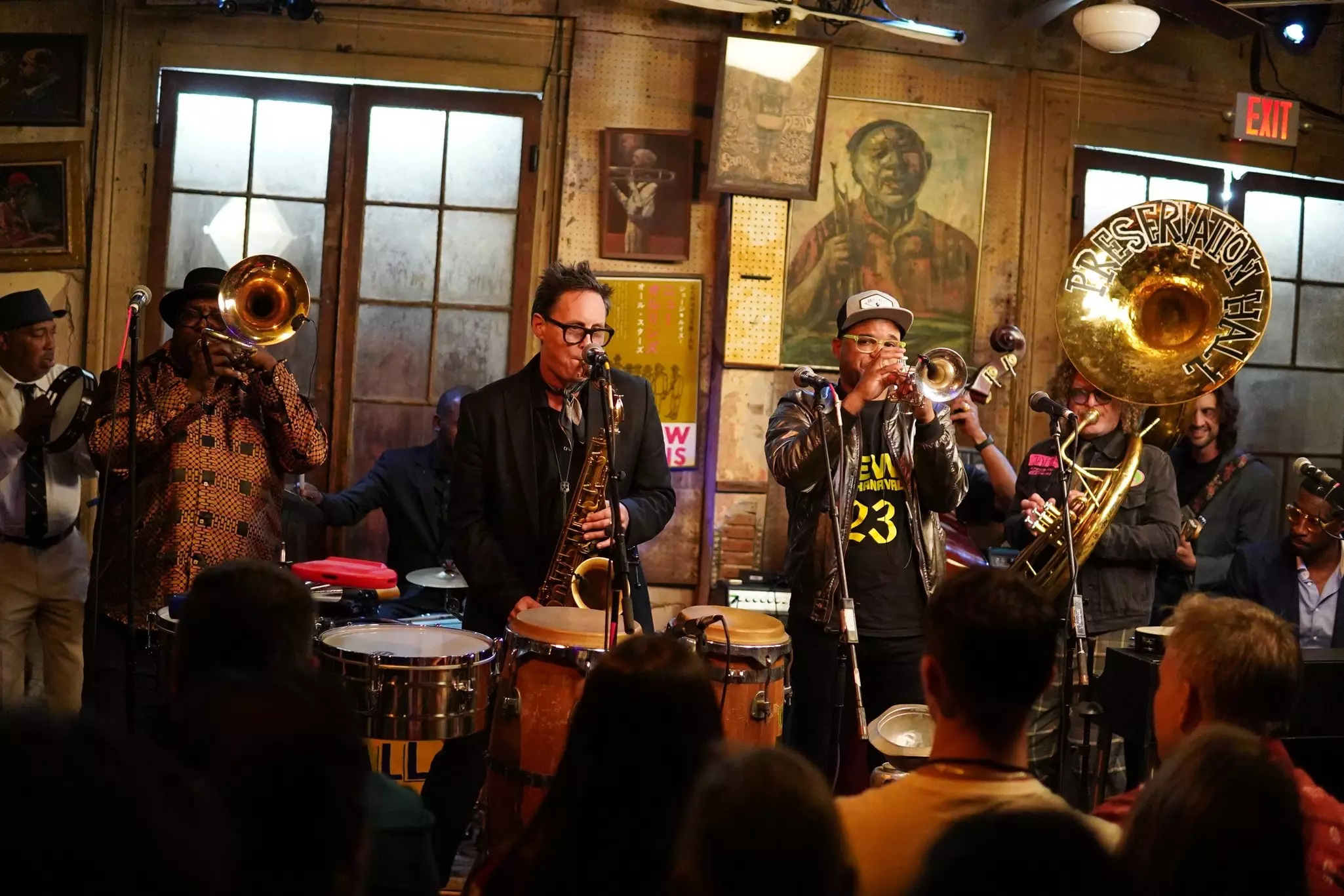 Horn players perform in a small venue as spectators look on.