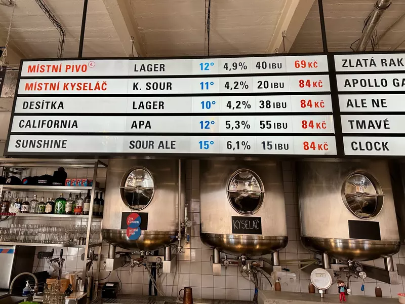 A large menu with words written in Czech and in English hanging over beer taps 