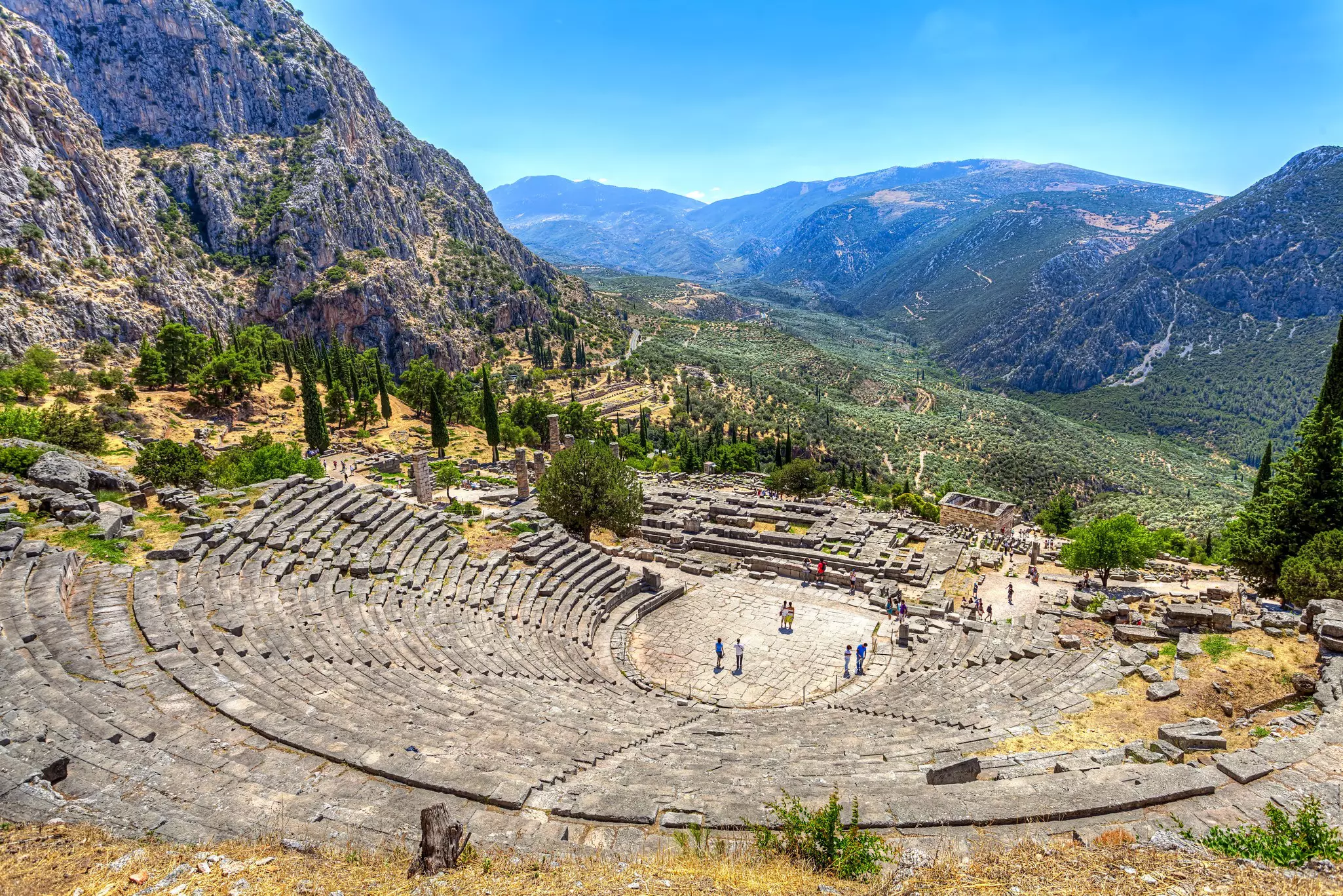 Tourists visit an ancient amphitheater surrounded by mountains.