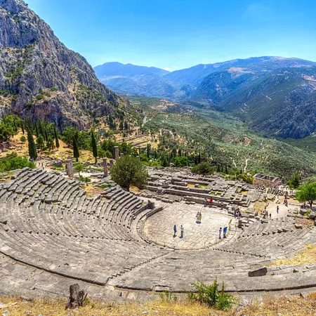 An aerial view of an ancient amphitheater built into a hillside. Mountains and a valley can be seen in the distance.