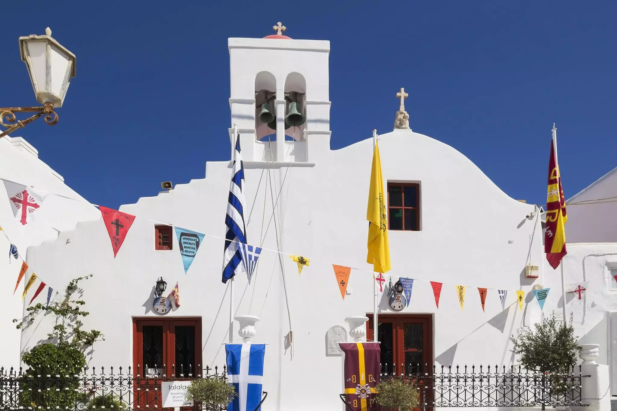 Greek Orthodox church and colorful flags hanging over narrow alley in Mykonos Hora, Greece.