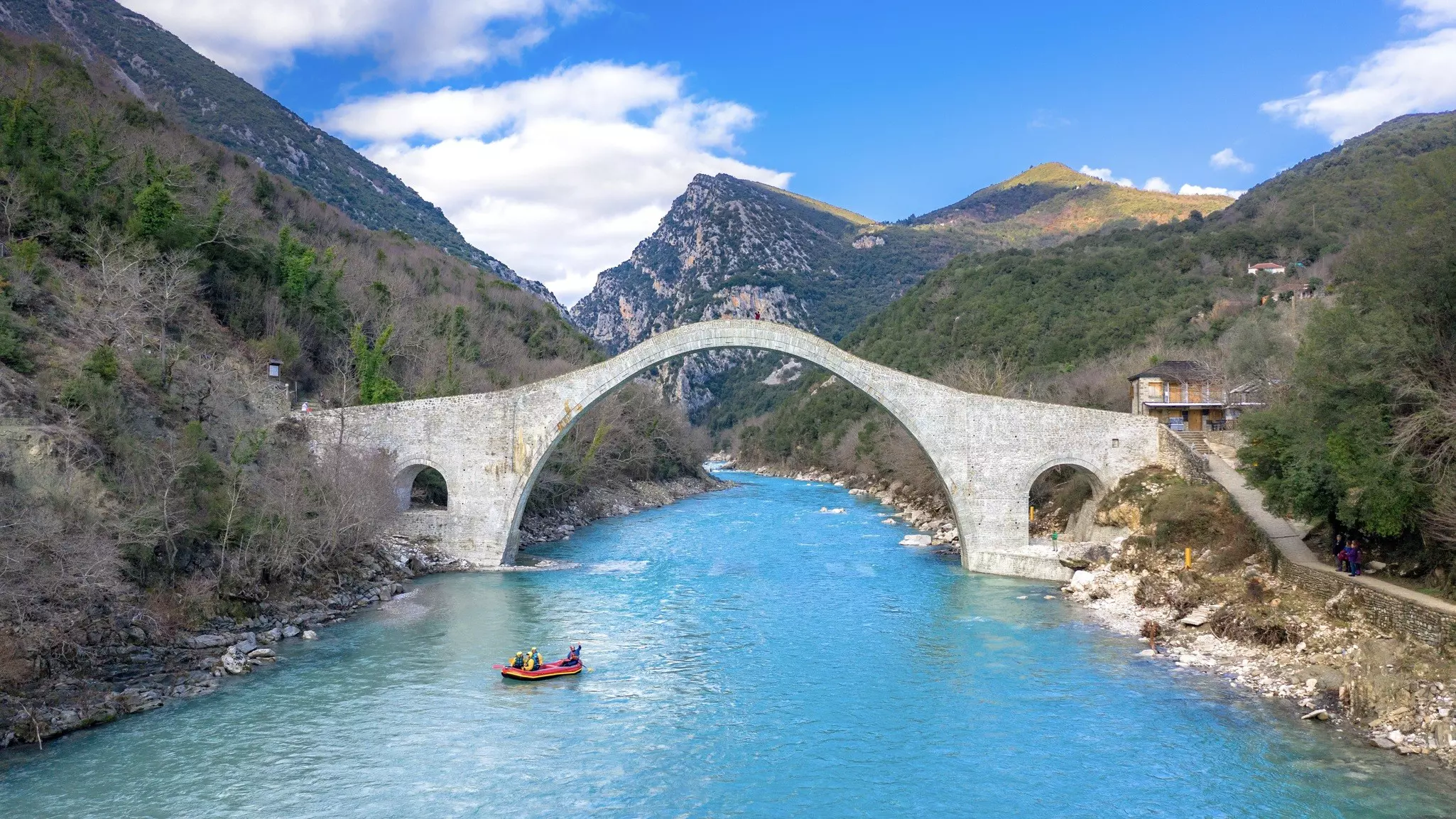 People raft in a very blue river under a curved arch stone bridge
