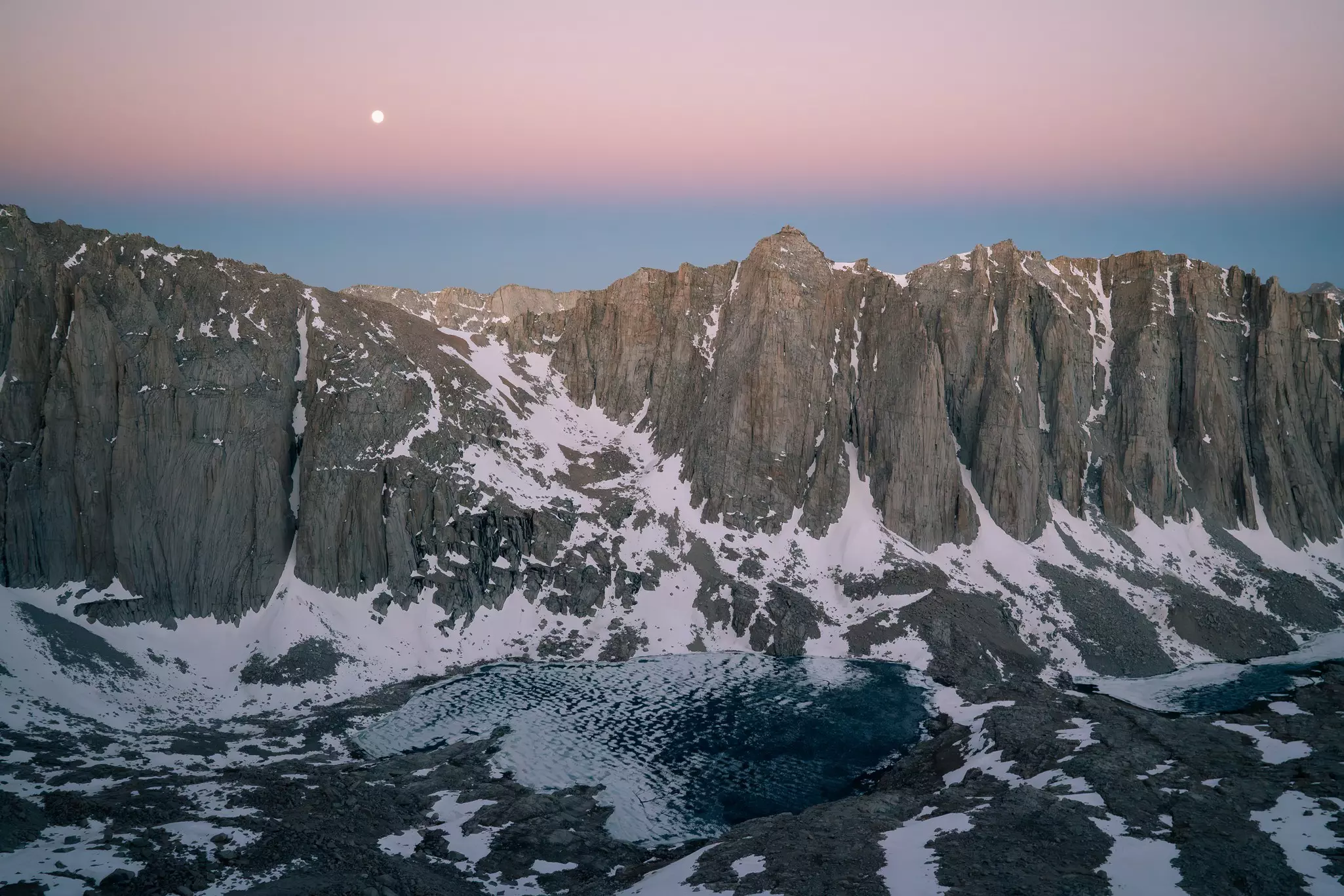 A chain of craggy mountains with patches of snow at sunrise.
