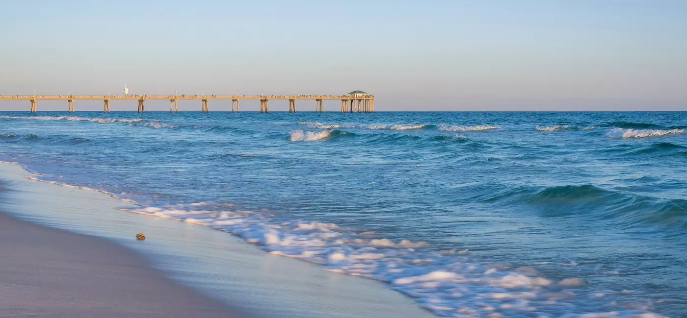  Okaloosa island pier with orange hued sky in the horizon during sunset. The fishing pier has a wonderful view of the ocean with waves crashing