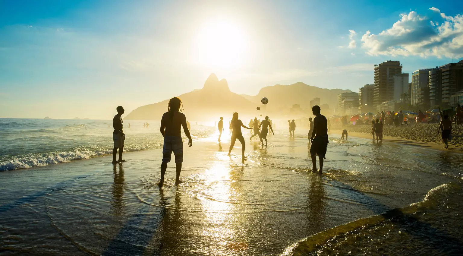 Distant sunset silhouettes playing keepy-uppie beach football on the sea shore in Ipanema Beach Rio de Janeiro Brazil