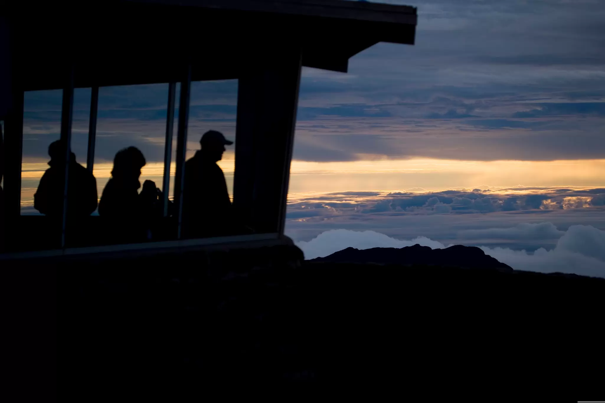 People stand at a lookout as the sun rises over a volcanic landscape;  Haleakalā National Park, Maui, Hawaii