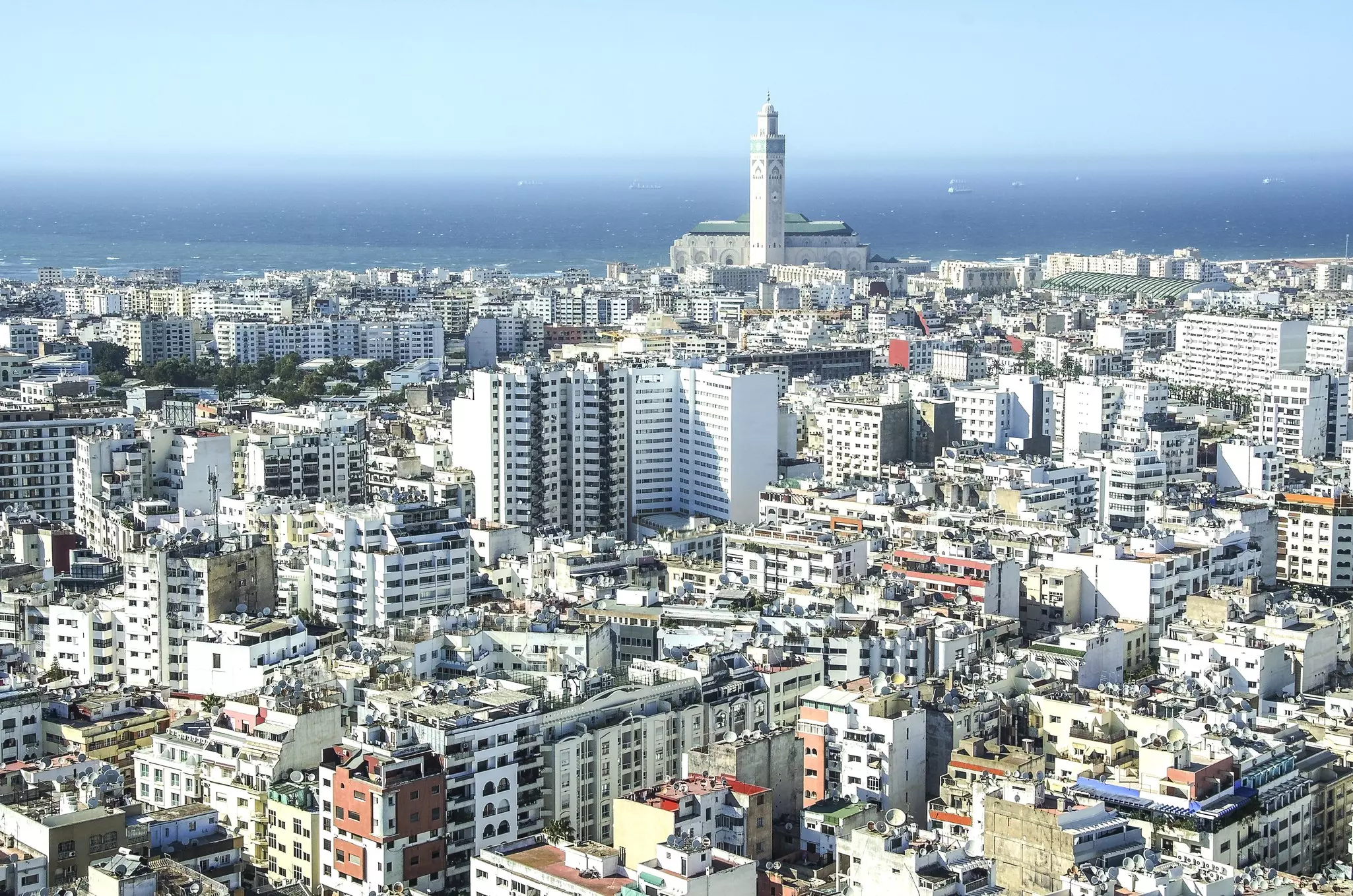 A coastal city with a the tall minaret of a mosque standing above many white buildings.