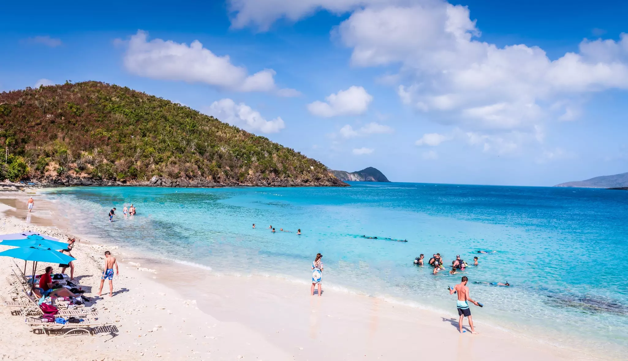 Snorkelers heading out into the shallows off a white-sand beach.