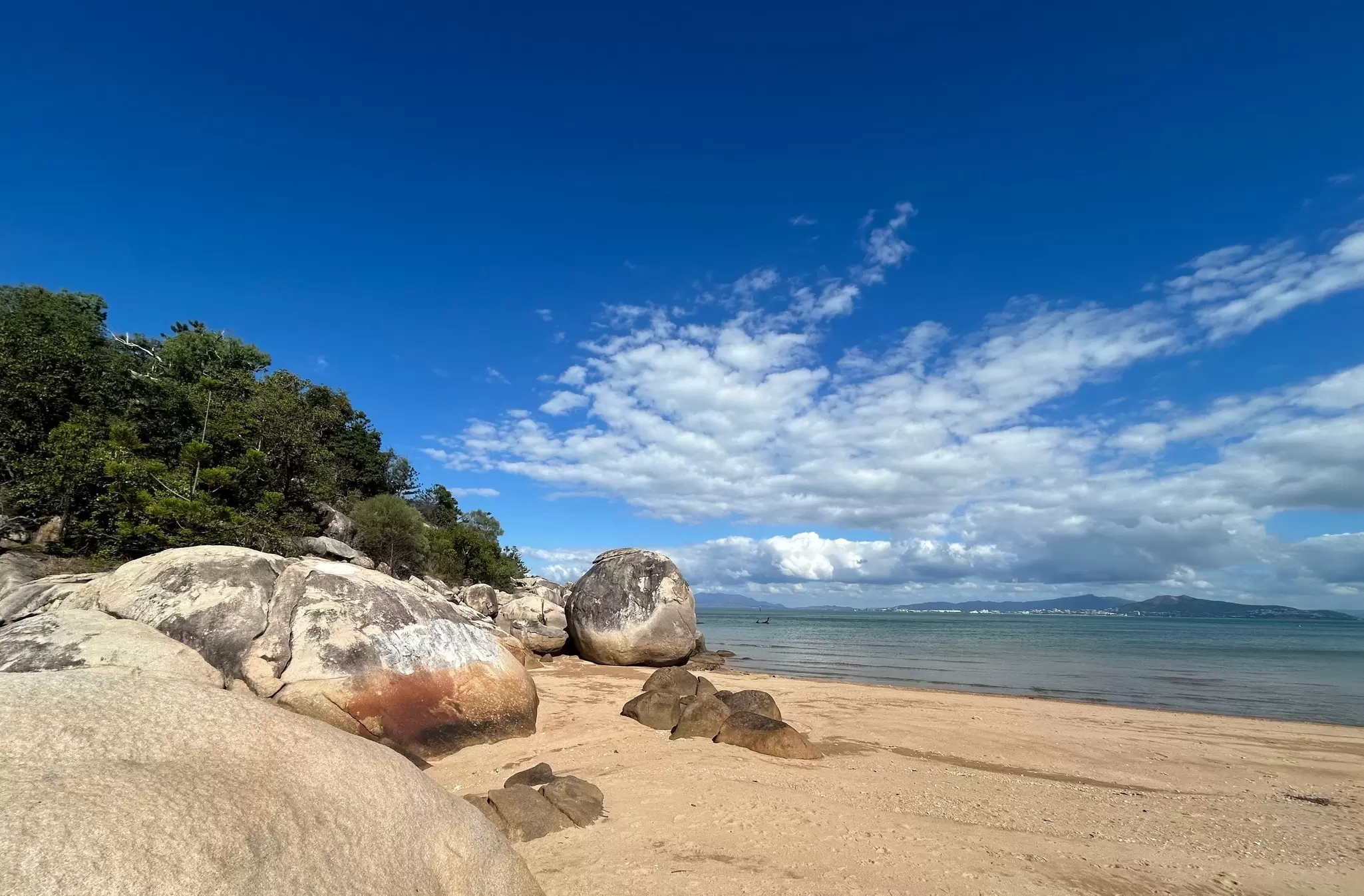 View of sea boulders and a distant shipwreck at Picnic Bay on Magnetic Island, Australia.