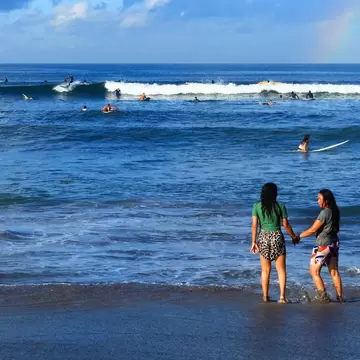 Canggu, Bali, Indonesia - March 16, 2022People standing on the beach and many surfers riding long boards on waves at Batu Bolong beach in Canggu, Bali with a rainbow in the sky., License Type: media, Download Time: 2026-02-06T17:35:53.000Z, User: meg3348277, Editorial: true, purchase_order: 56530 - Guidebooks, job: Global Publishing-WIP, client: Lonely Planet – Bali, Lombok & Nusa Tenggara 20, other: Megan Cassidy