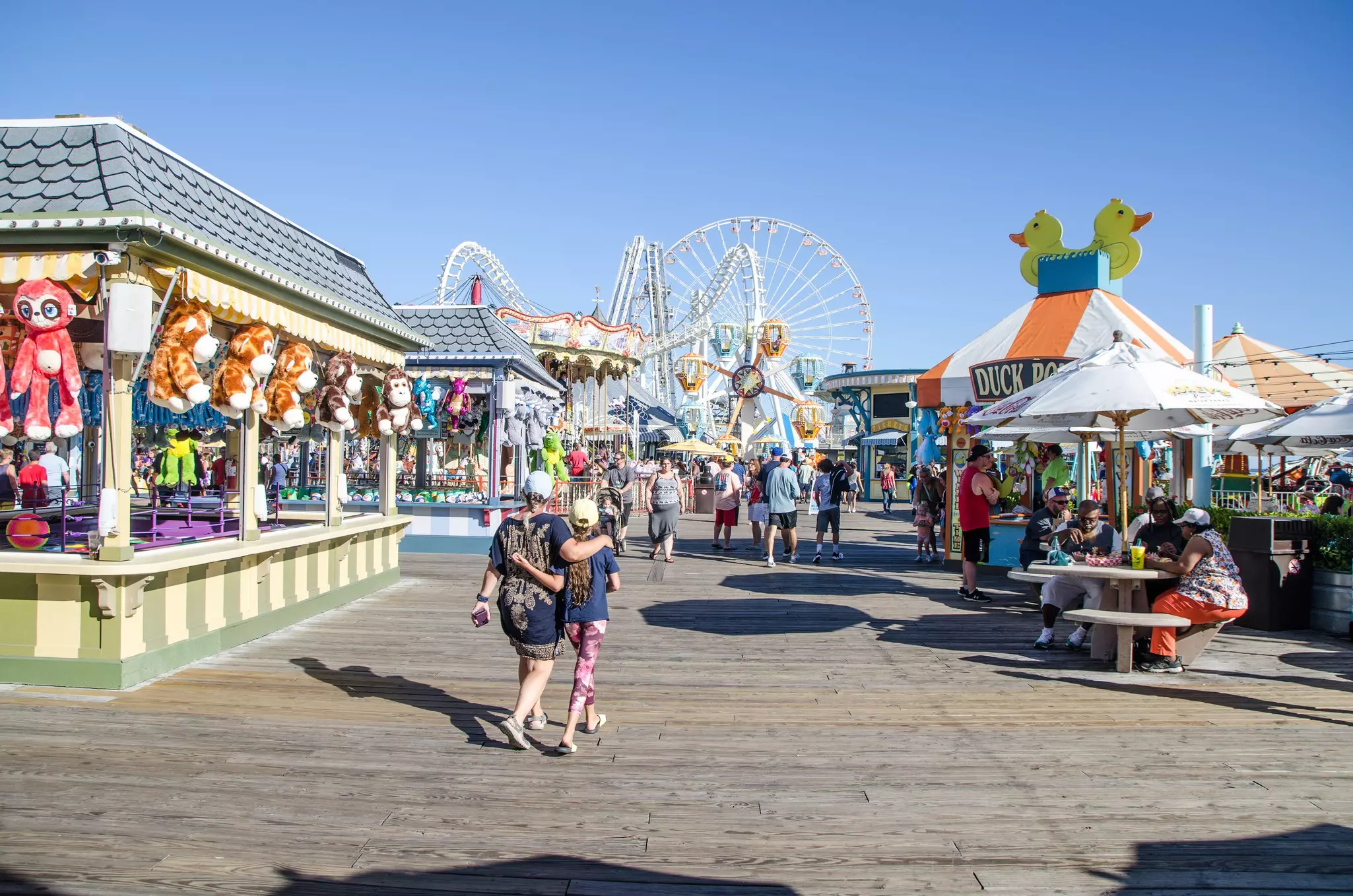 Two vacationers are walking through an amusement park with fairground games and rides in Wildwood, New Jersey
